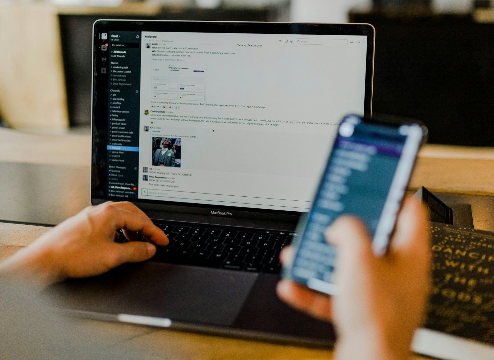 Person using a laptop and smartphone on a wooden desk